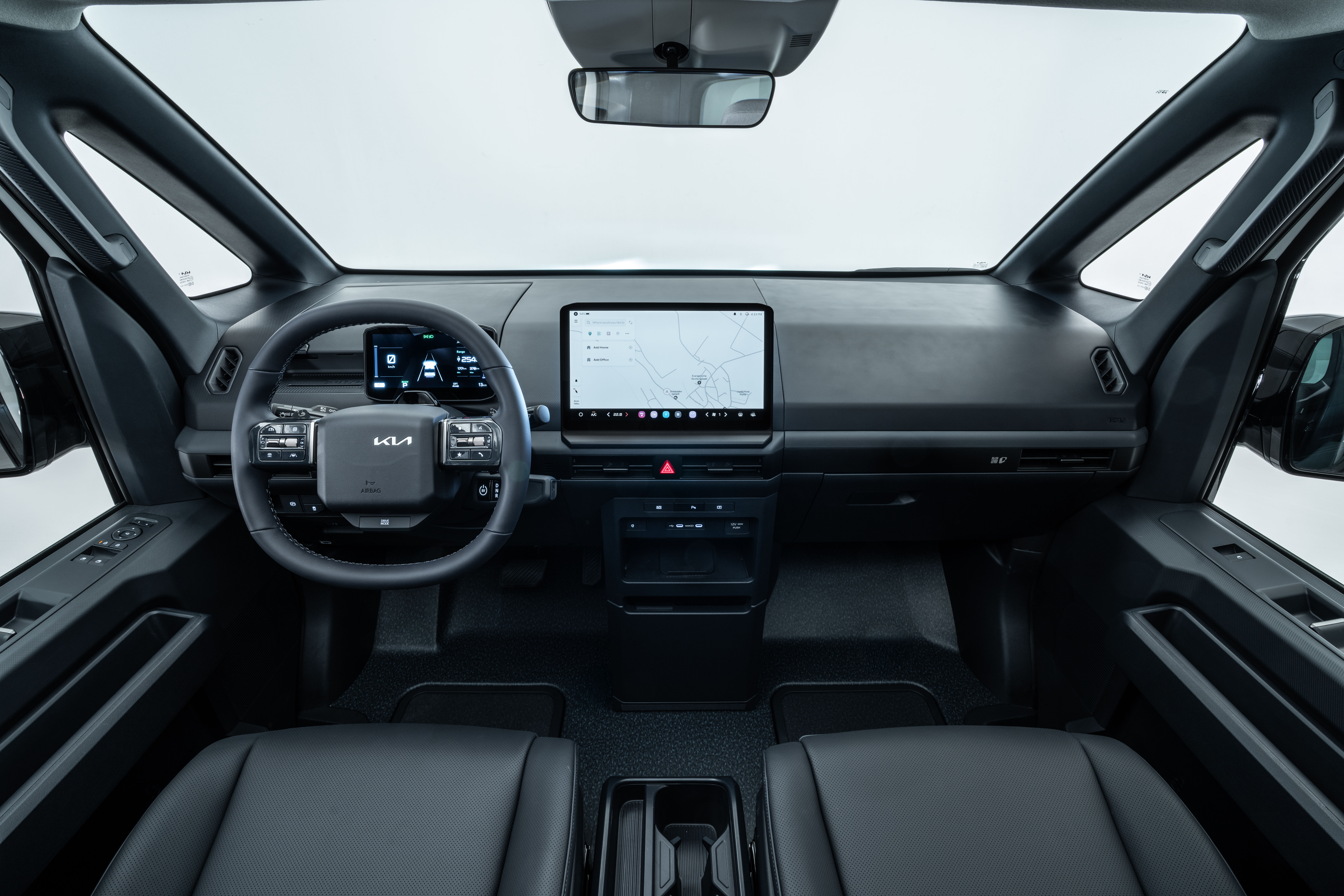 Interior del Kia PV5 Chasis Cabina con salpicadero, volante con logo Kia, panel de instrumentos digital, pantalla de infoentretenimiento y consola central.