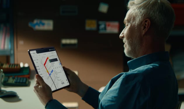 Un hombre consultando una tablet que muestra un mapa con una ruta planificada en un entorno de oficina.