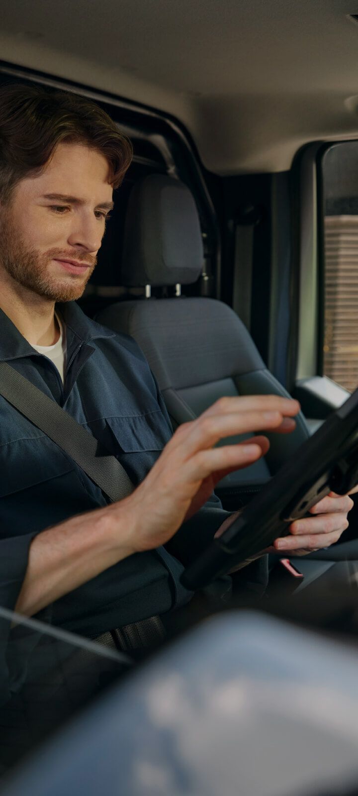 Conductor sentado al volante de un vehículo comercial ligero, con asiento gris e interior oscuro.