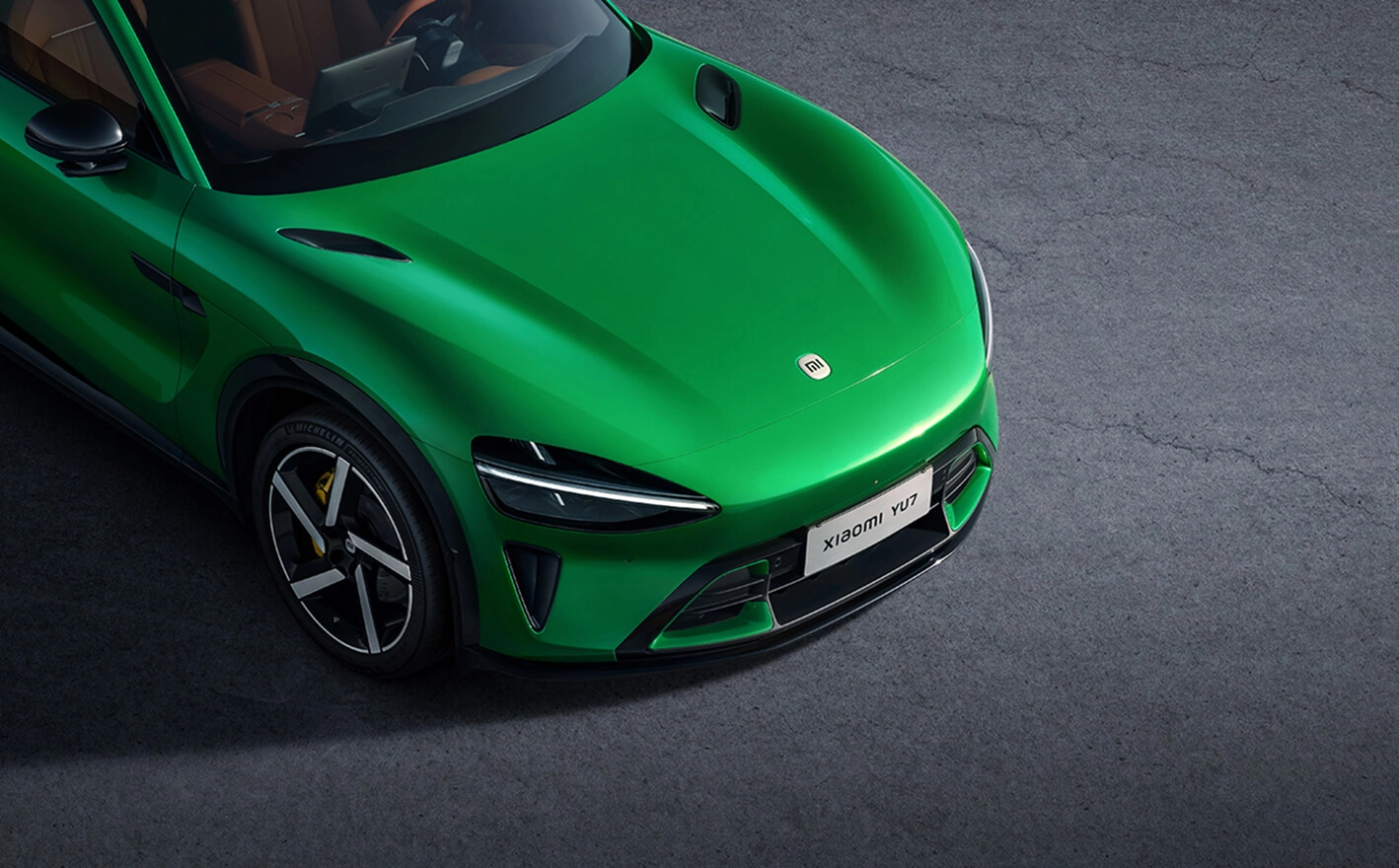 Vista frontal-superior del Xiaomi YU7 verde: capó, faro izquierdo y parrilla, con llanta multirradio bicolor y pinza amarilla