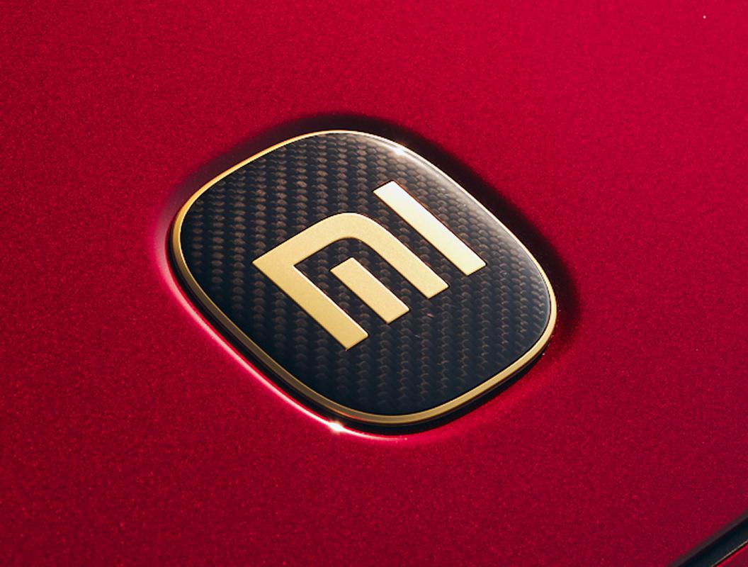 Emblema Xiaomi en fibra de carbono con borde dorado sobre pintura roja metalizada, seña del acabado GT
