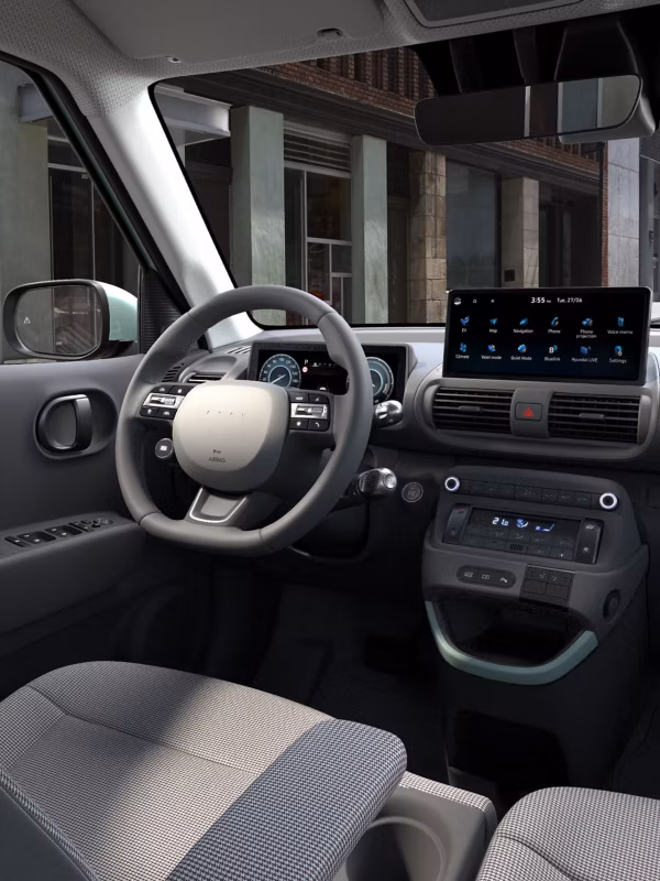 Interior del Hyundai Inster con el salpicadero, el volante, la pantalla central y asientos con tapicería de patrón houndstooth