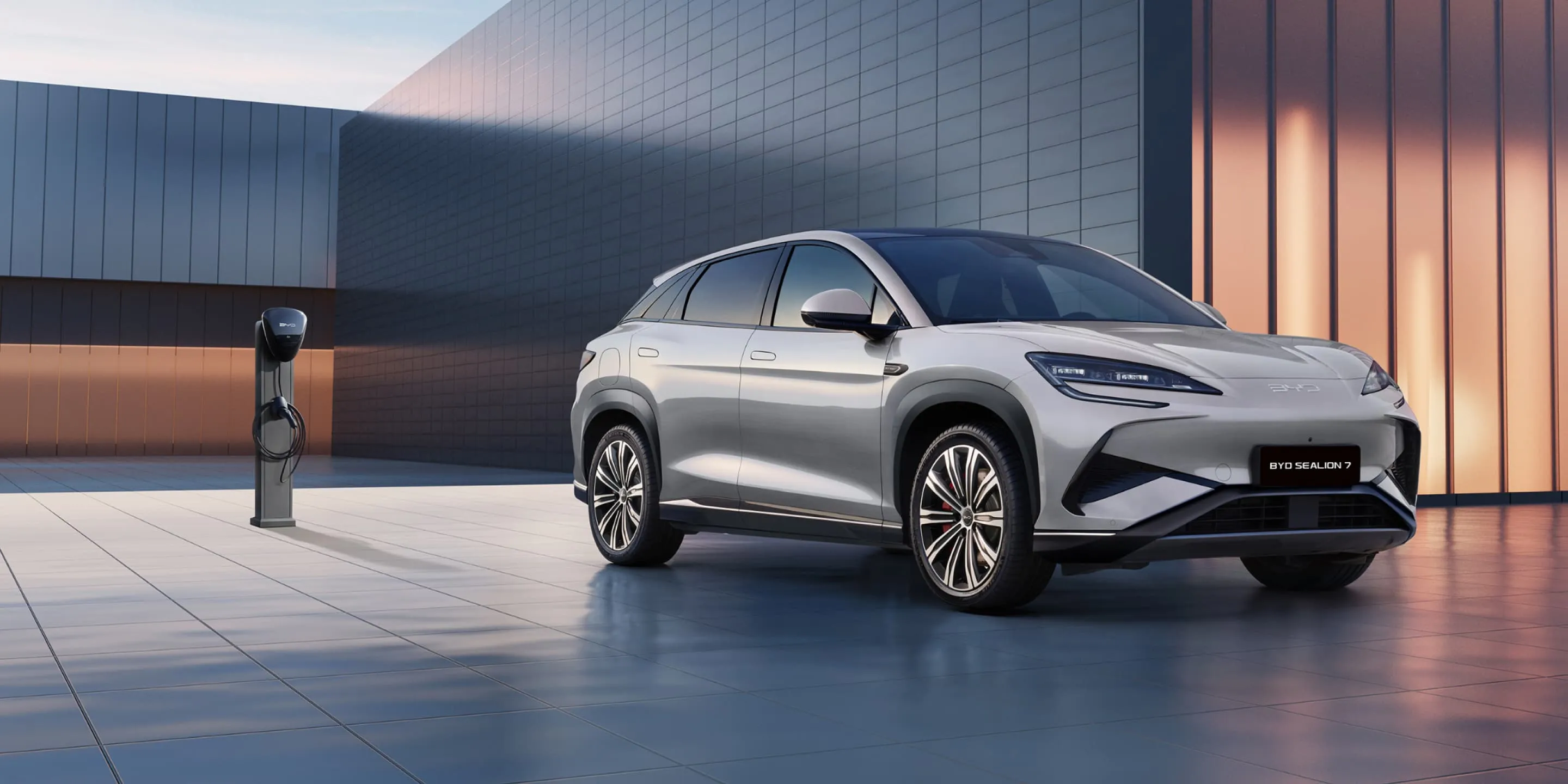BYD Sealion 7 gris plata aparcado junto a un punto de carga en un entorno arquitectónico moderno