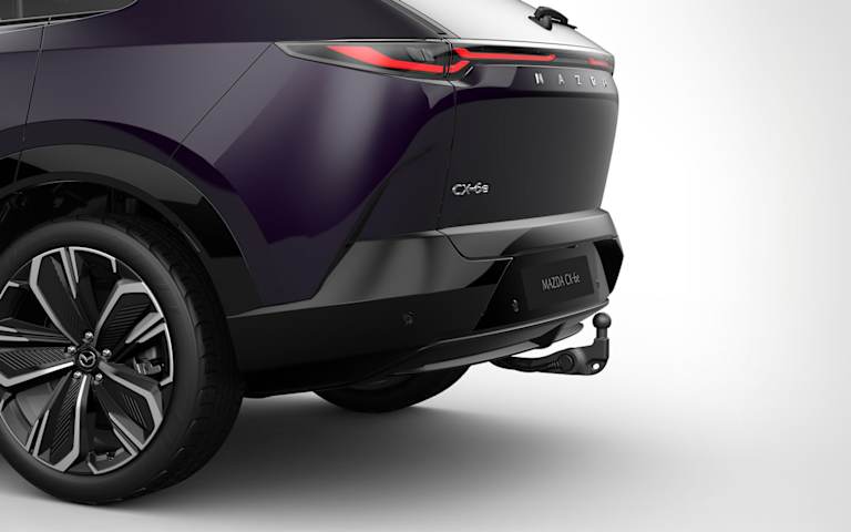 Vista trasera tres cuartos del CX-6e morado oscuro con la bola de remolque desplegada.