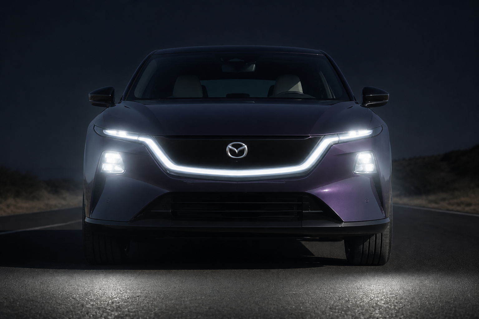 La misma toma frontal del CX-6e de noche, con los faros LED encendidos proyectando un halo de luz sobre el asfalto.