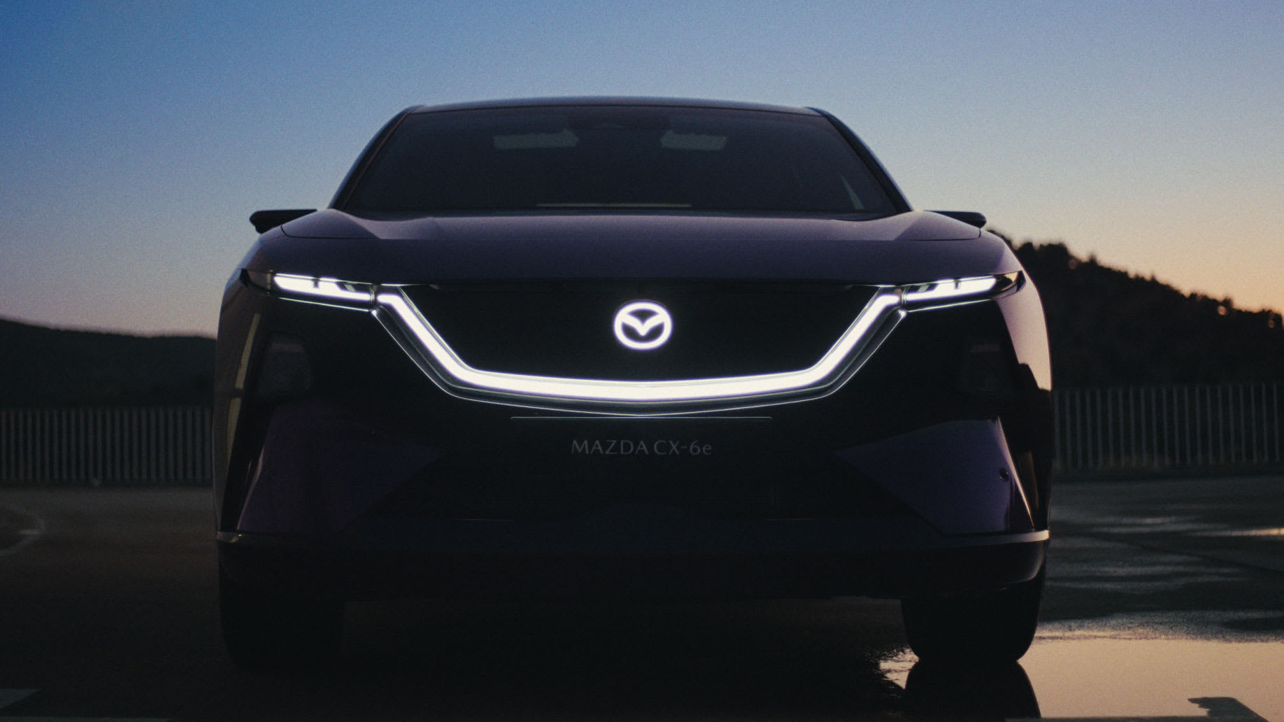 Vista frontal del Mazda CX-6e en color morado oscuro sobre fondo claro, con la denominación del modelo visible en el frontal.