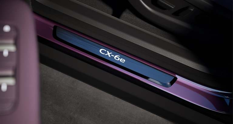 Umbral de puerta iluminado con el logotipo CX-6e en blanco sobre panel azul y moldura metálica oscura.