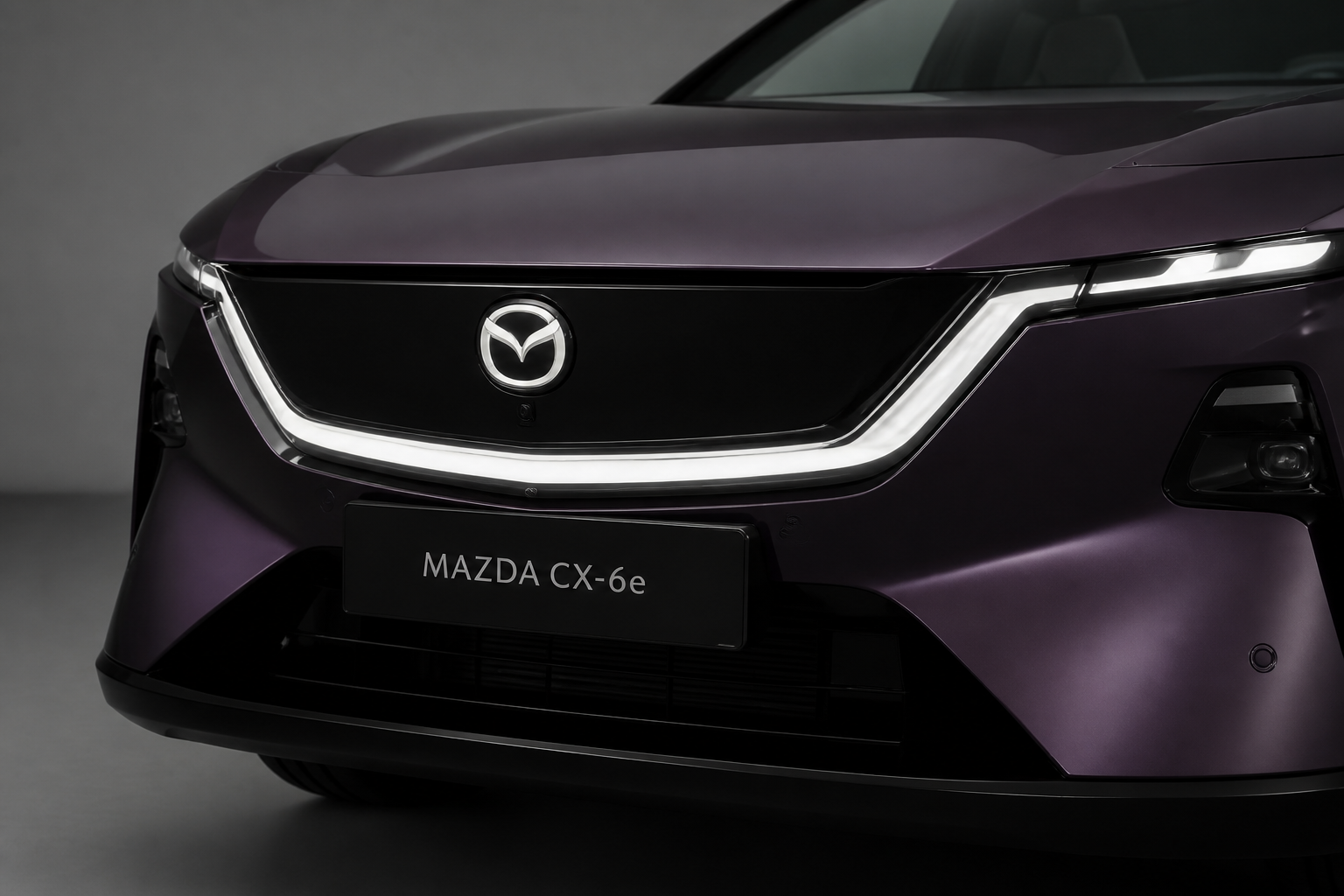 Primer plano del frontal del CX-6e en la zona del emblema donde se integran los sensores, en estudio neutro.