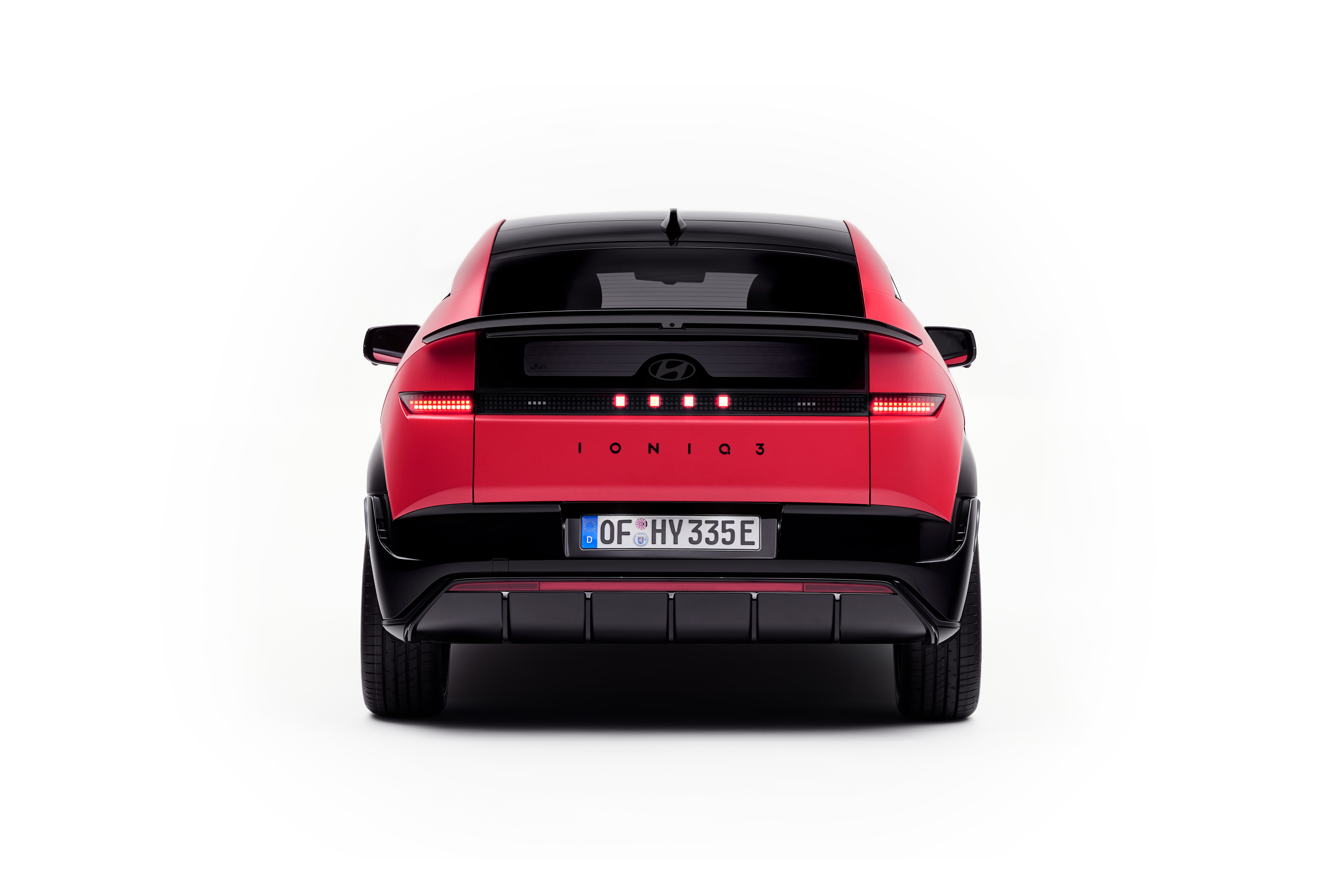 Vista trasera del IONIQ 3 rojo con techo negro y luces traseras LED encendidas sobre fondo blanco