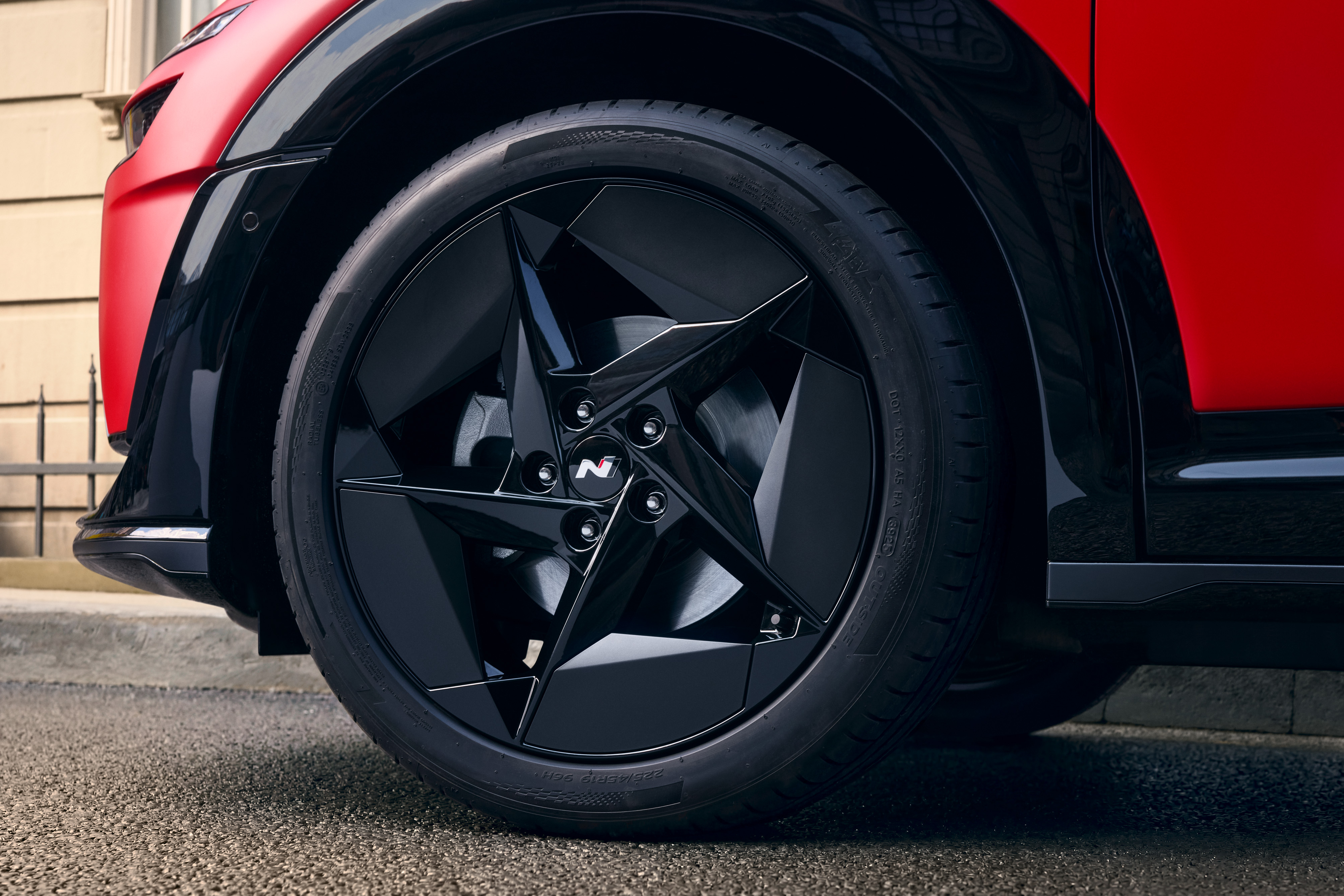 Detalle de la llanta de aleación negra de cinco radios y el paso de rueda de un vehículo rojo