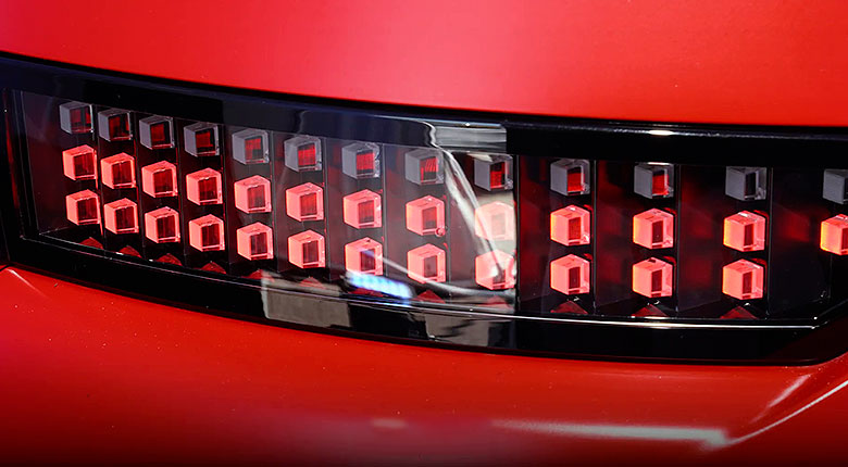 Vista trasera del IONIQ 3 rojo con techo negro y luces traseras LED encendidas sobre fondo blanco