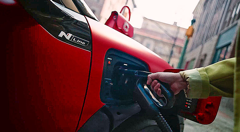 Primer plano del puerto de carga abierto del IONIQ 3 rojo con un conector de carga rápida enchufado