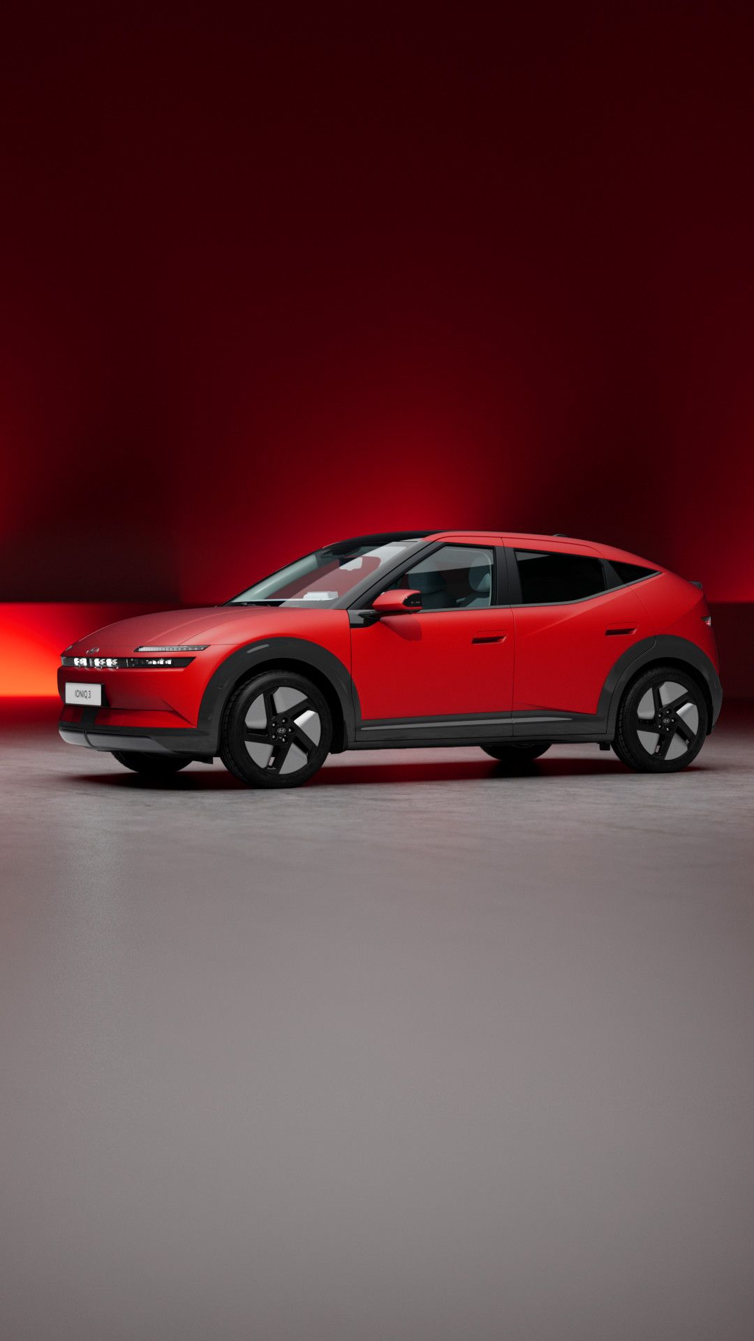 Hyundai IONIQ 3 rojo en un estudio con fondo rojo, visto en tres cuartos frontal