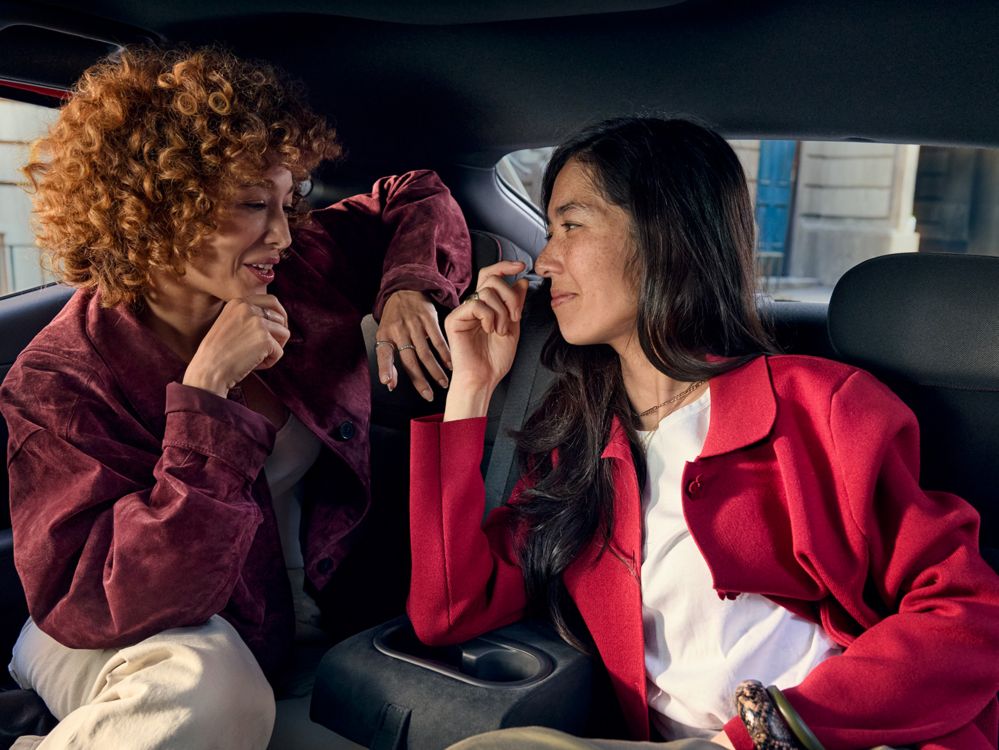 Dos mujeres conversando en los asientos traseros, con la consola de portavasos entre ellas