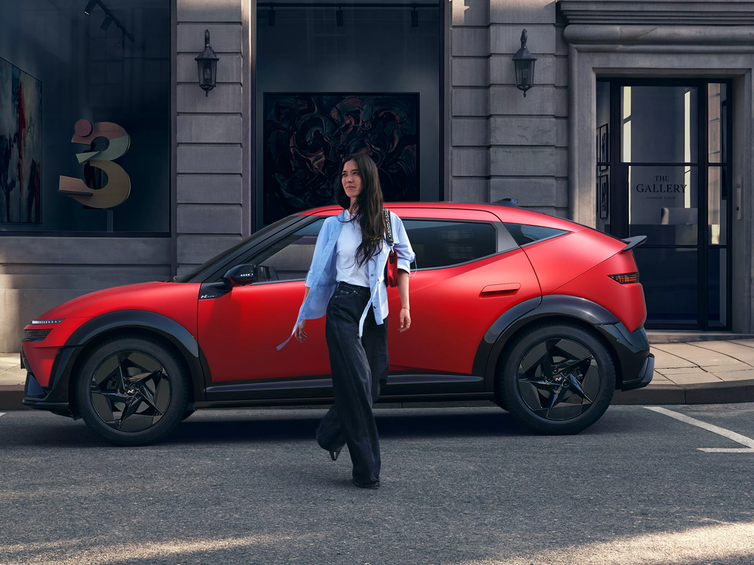 Smartphone con una app de servicios del vehículo con iconos abstractos y, al fondo desenfocado, el IONIQ 3 rojo aparcado