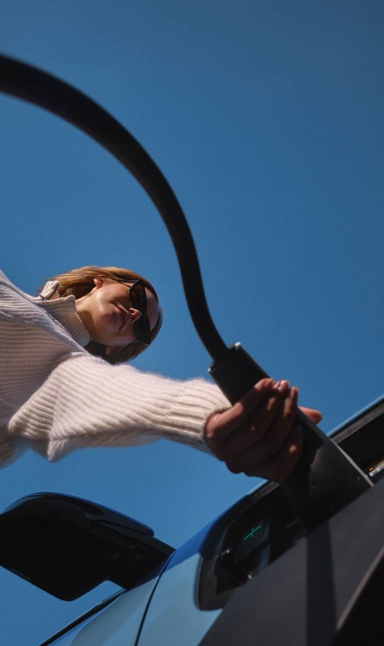 Primer plano de una persona conectando el cargador al puerto de carga del coche eléctrico
