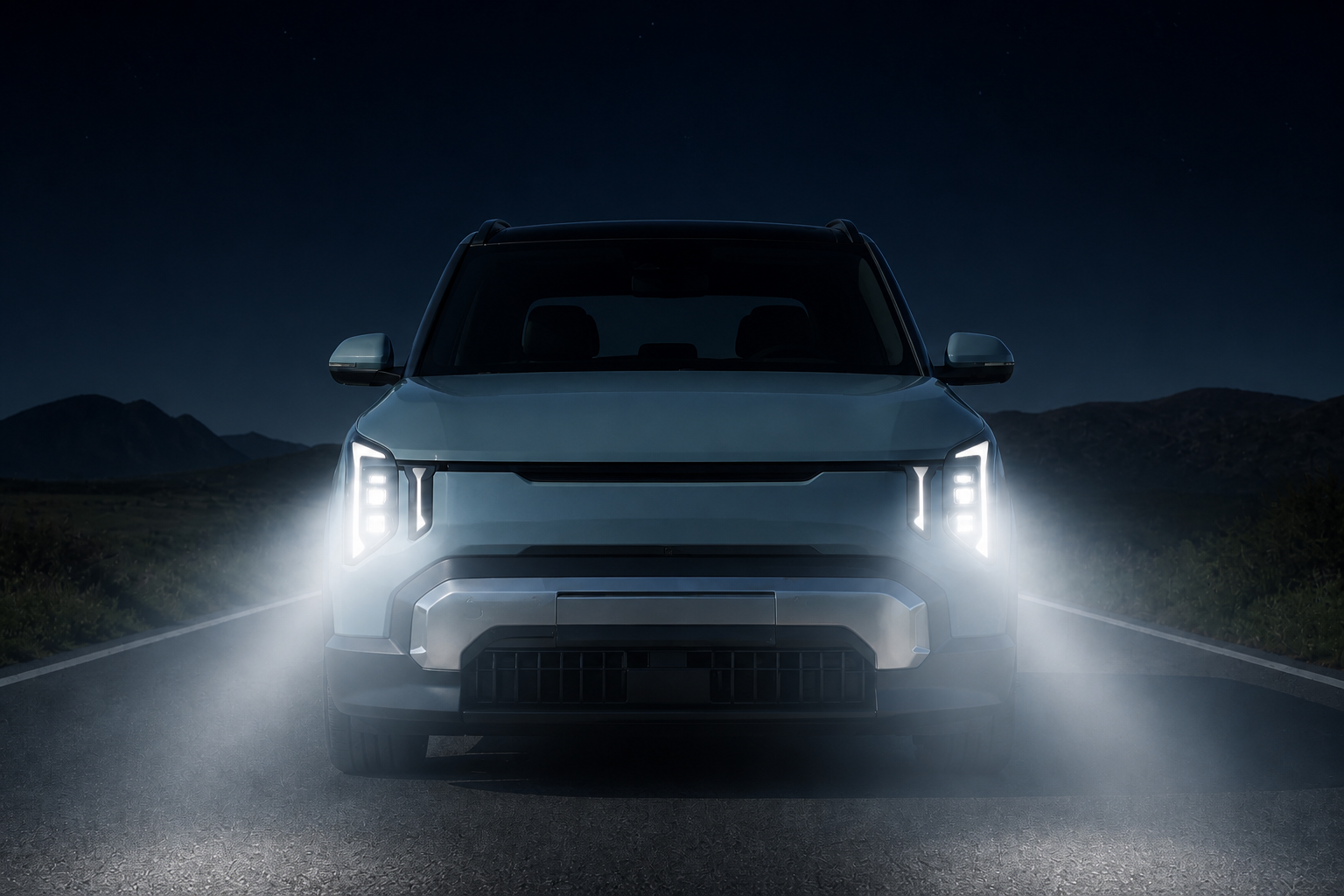 El mismo frontal del Kia EV2 de noche con los faros encendidos proyectando luz sobre la carretera