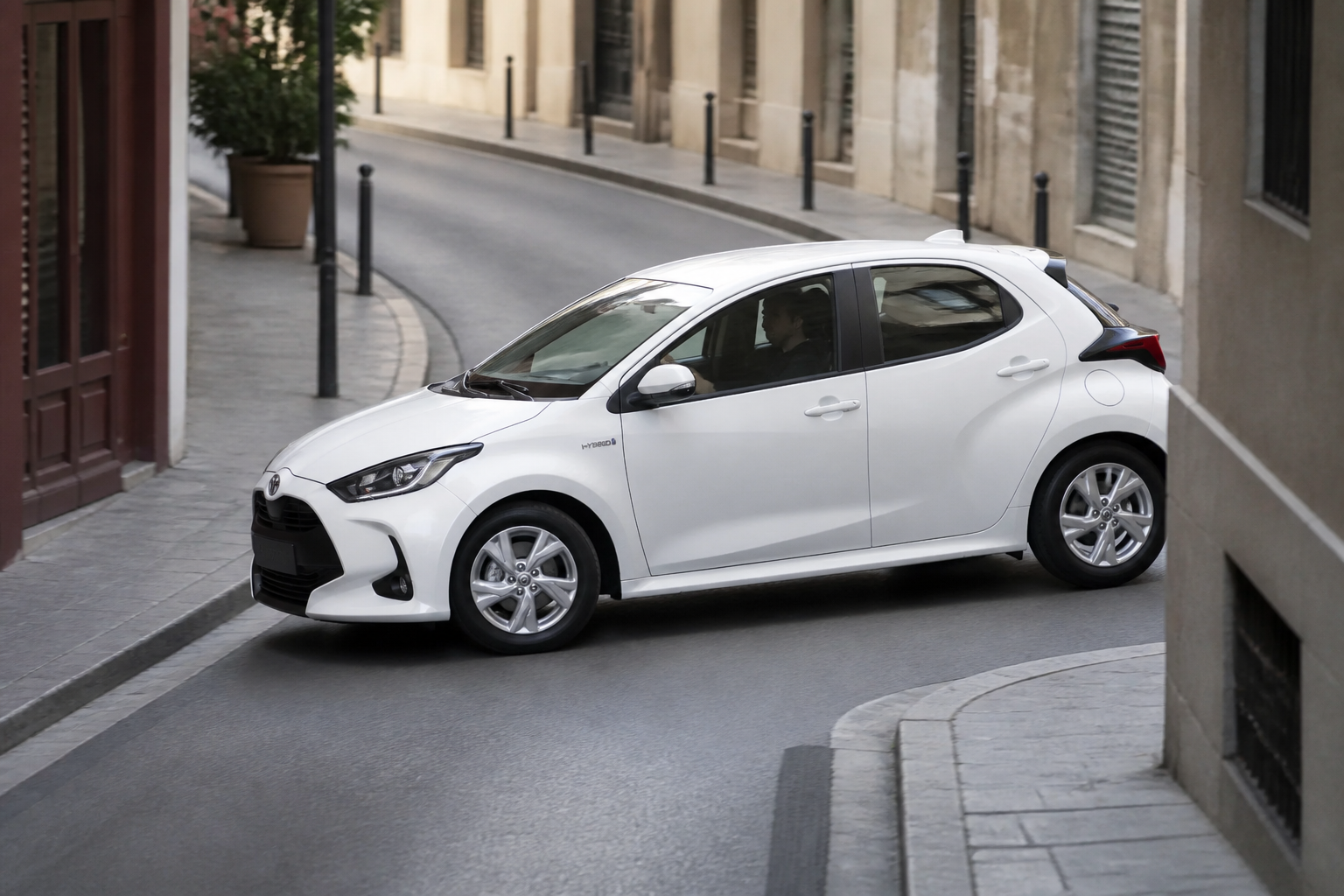 Toyota Yaris blanco maniobrando en una calle estrecha de ciudad, visto desde un punto elevado