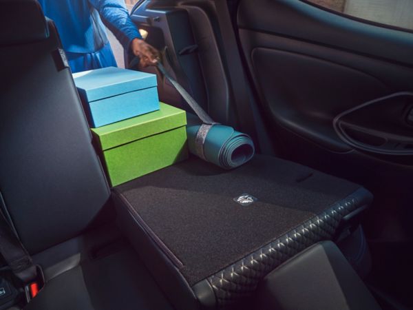 Asientos traseros abatidos con cajas y una colchoneta mientras una persona carga objetos en el coche