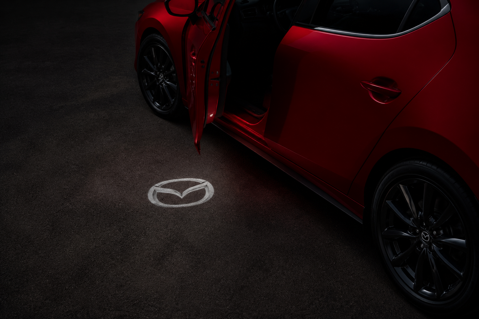 Puerta delantera entreabierta de noche proyectando el logotipo Mazda iluminado sobre el asfalto