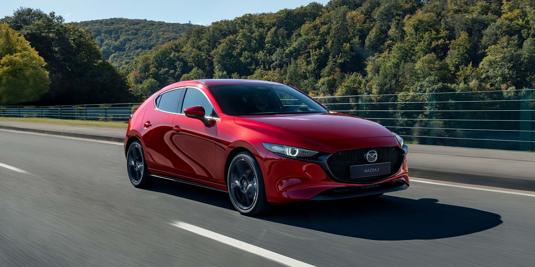 Mazda3 hatchback rojo conduciendo por una carretera entre árboles verdes