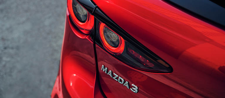 Acercamiento a la luz trasera y el emblema de un Mazda3 de color rojo
