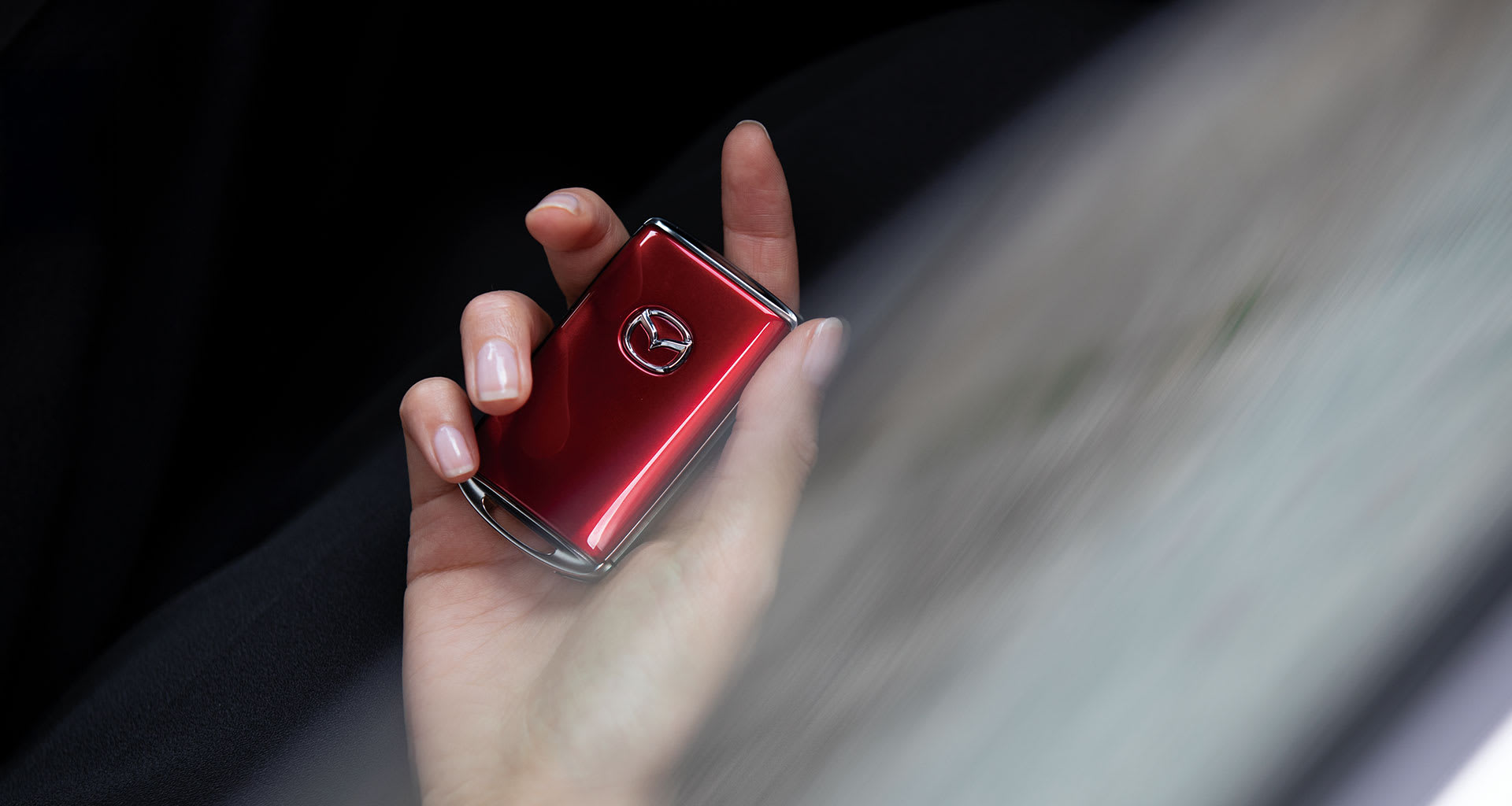 Una mano sostiene una llave Mazda de color rojo oscuro con el logotipo visible
