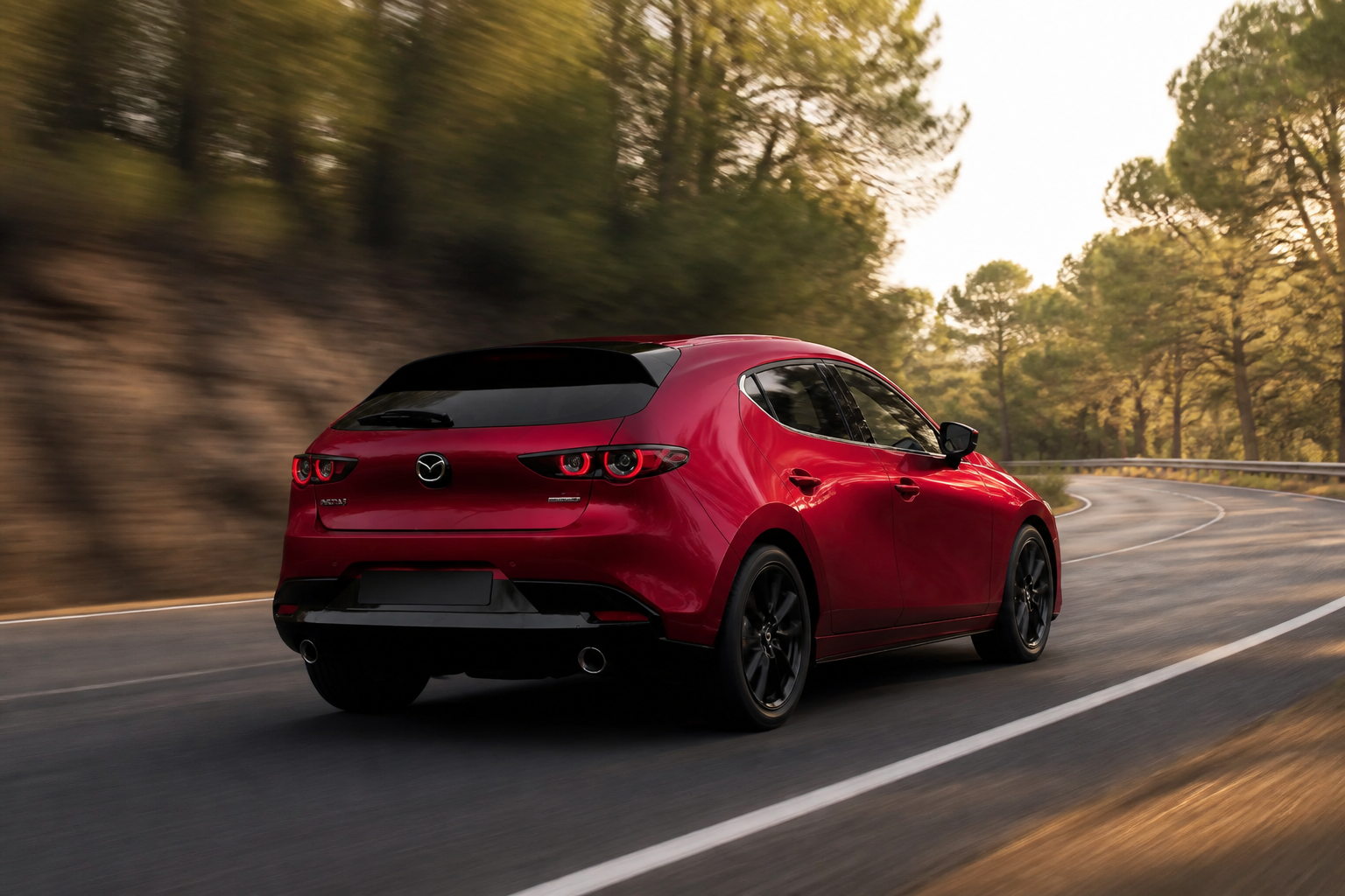 Tres cuartos trasero del Mazda3 rojo avanzando por una carretera de curvas entre árboles