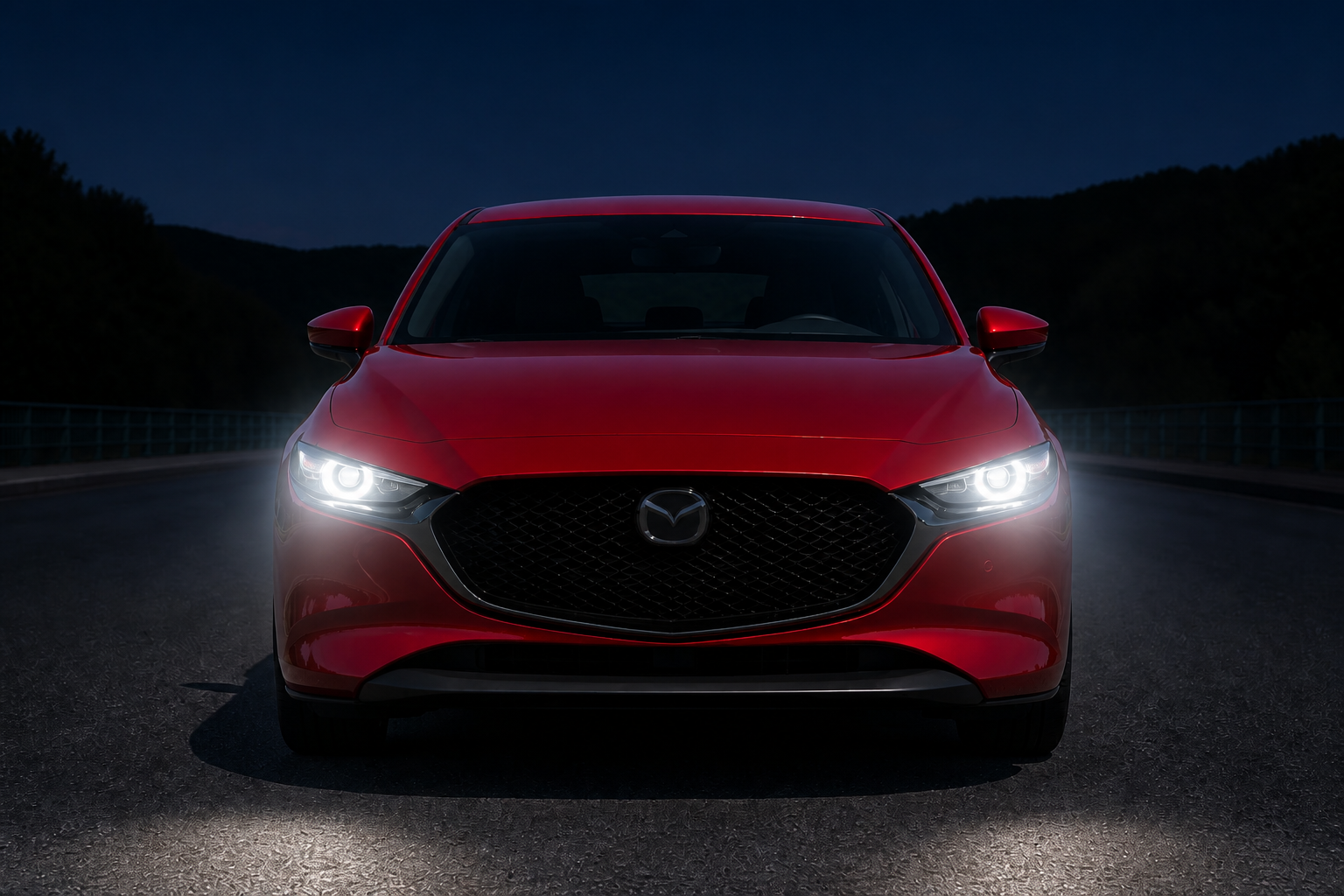 La misma toma frontal del Mazda3 de noche, con los faros LED encendidos proyectando su halo sobre la carretera
