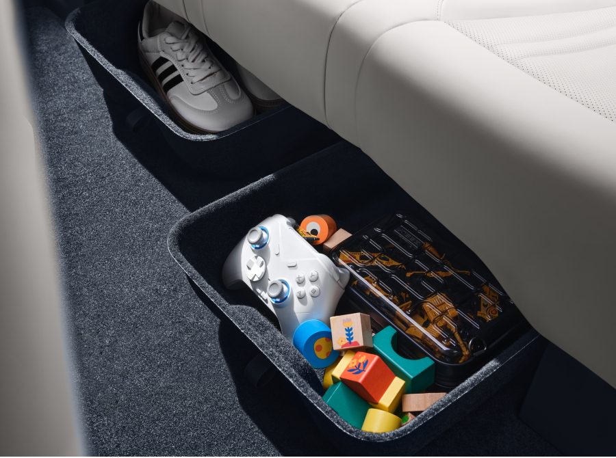 Bandejas de almacenamiento en el suelo del habitáculo con zapatillas, un mando de videojuegos y juguetes