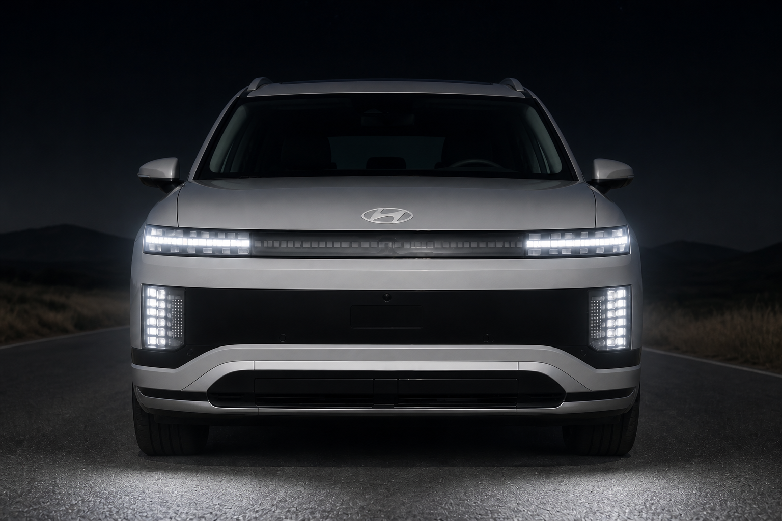 El mismo frontal del IONIQ 9 de noche con los faros LED encendidos proyectando luz sobre la carretera