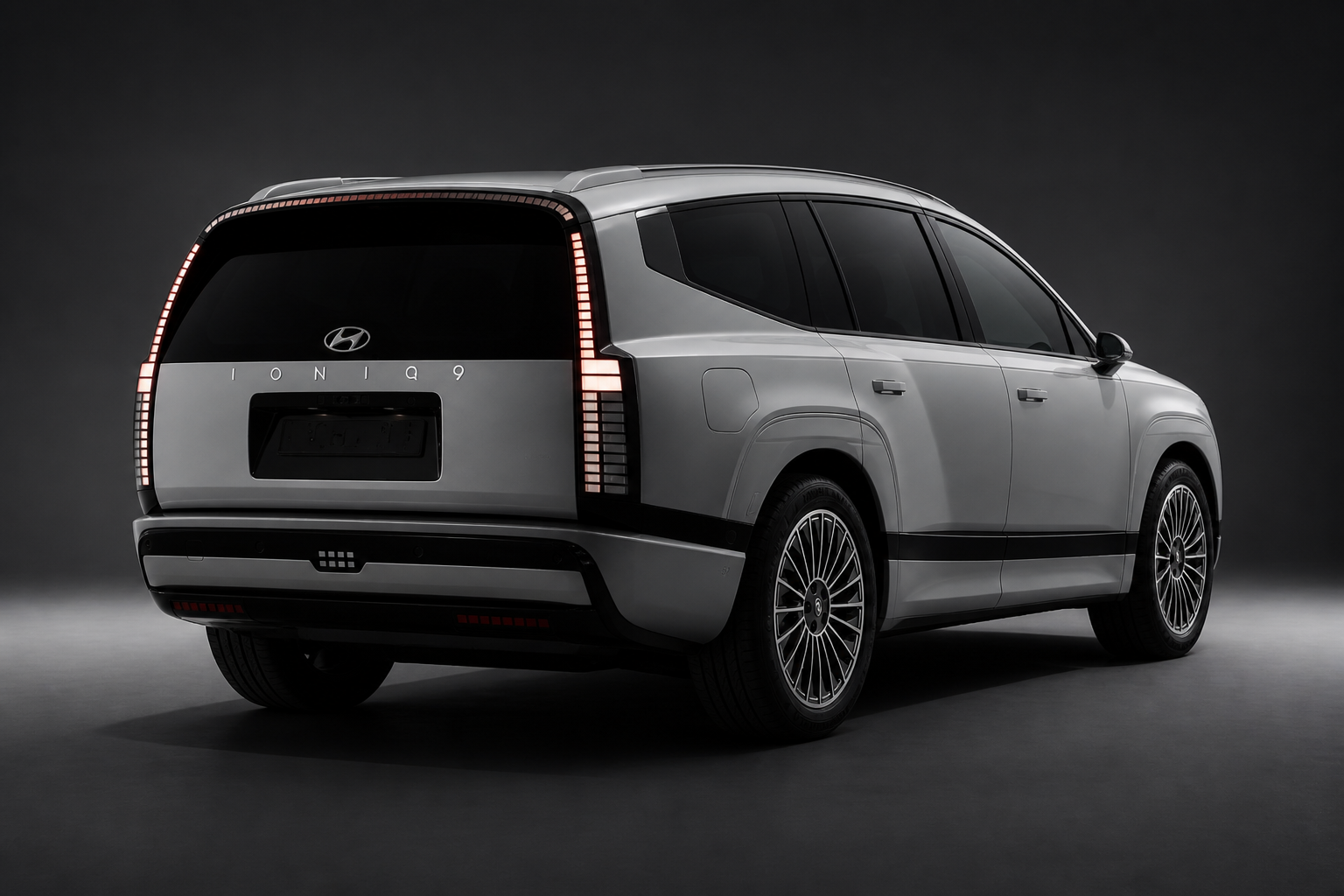 IONIQ 9 gris claro en tres cuartos trasero en estudio oscuro con portón y emblema en negro brillante