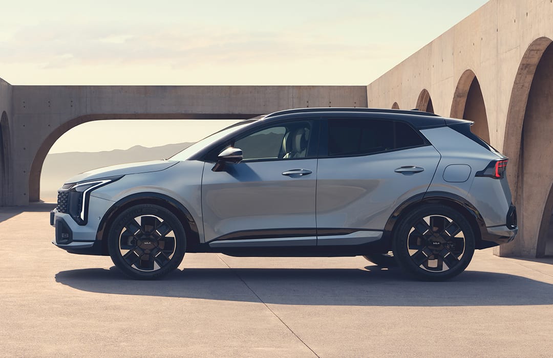 Vista lateral del Kia Sportage gris claro con techo negro junto a una arquitectura de arcos de hormigón