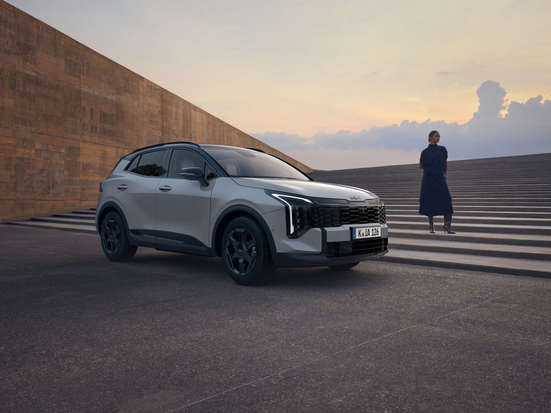 Kia Sportage gris claro aparcado al atardecer con una persona al fondo sobre unas escaleras