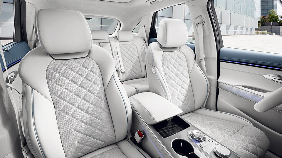 Interior del Electrified GV70 con asientos blancos acolchados, detalles en azul pálido en las puertas y consola central con mandos rotatorios.