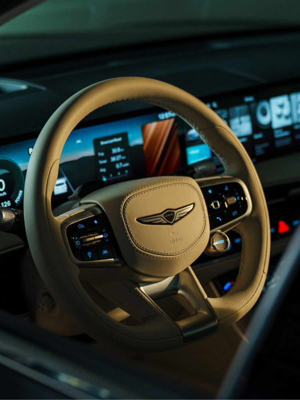 Volante del Electrified GV70 en tono claro con el emblema Genesis, botones de control y parte del cuadro digital.