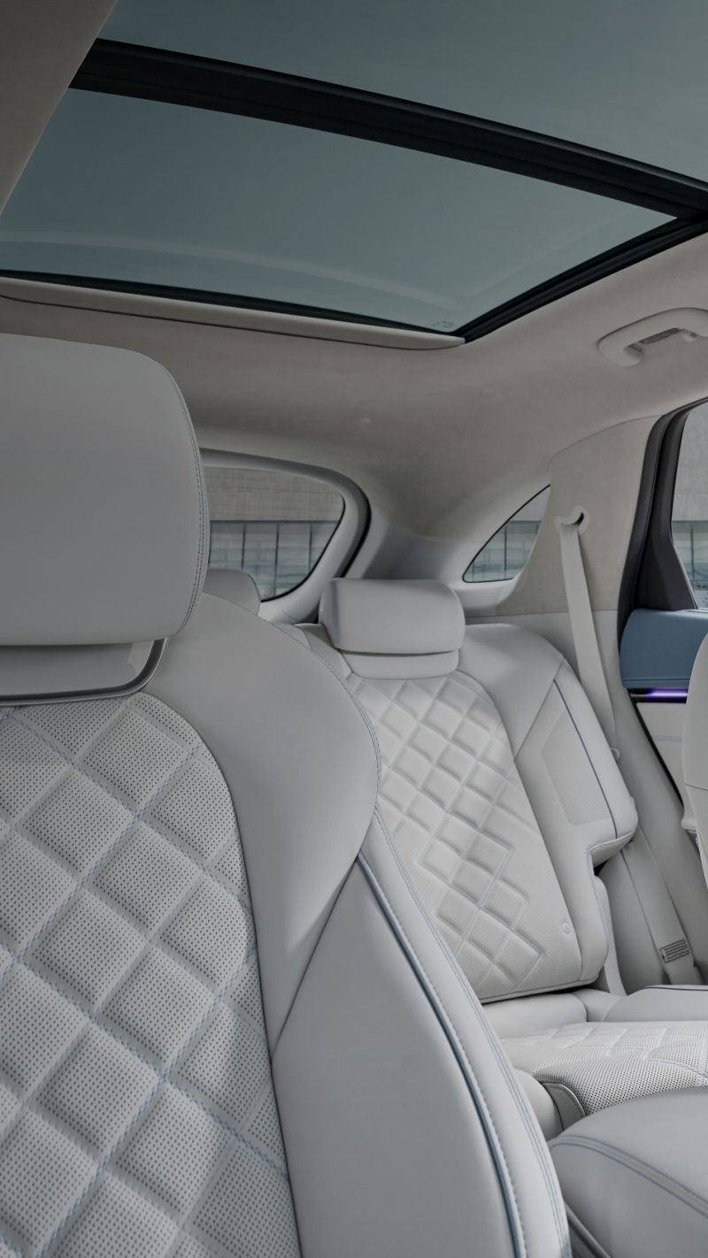 Asiento del pasajero delantero en cuero gris claro acolchado y perforado con costuras azules; al fondo, asientos traseros y techo panorámico.