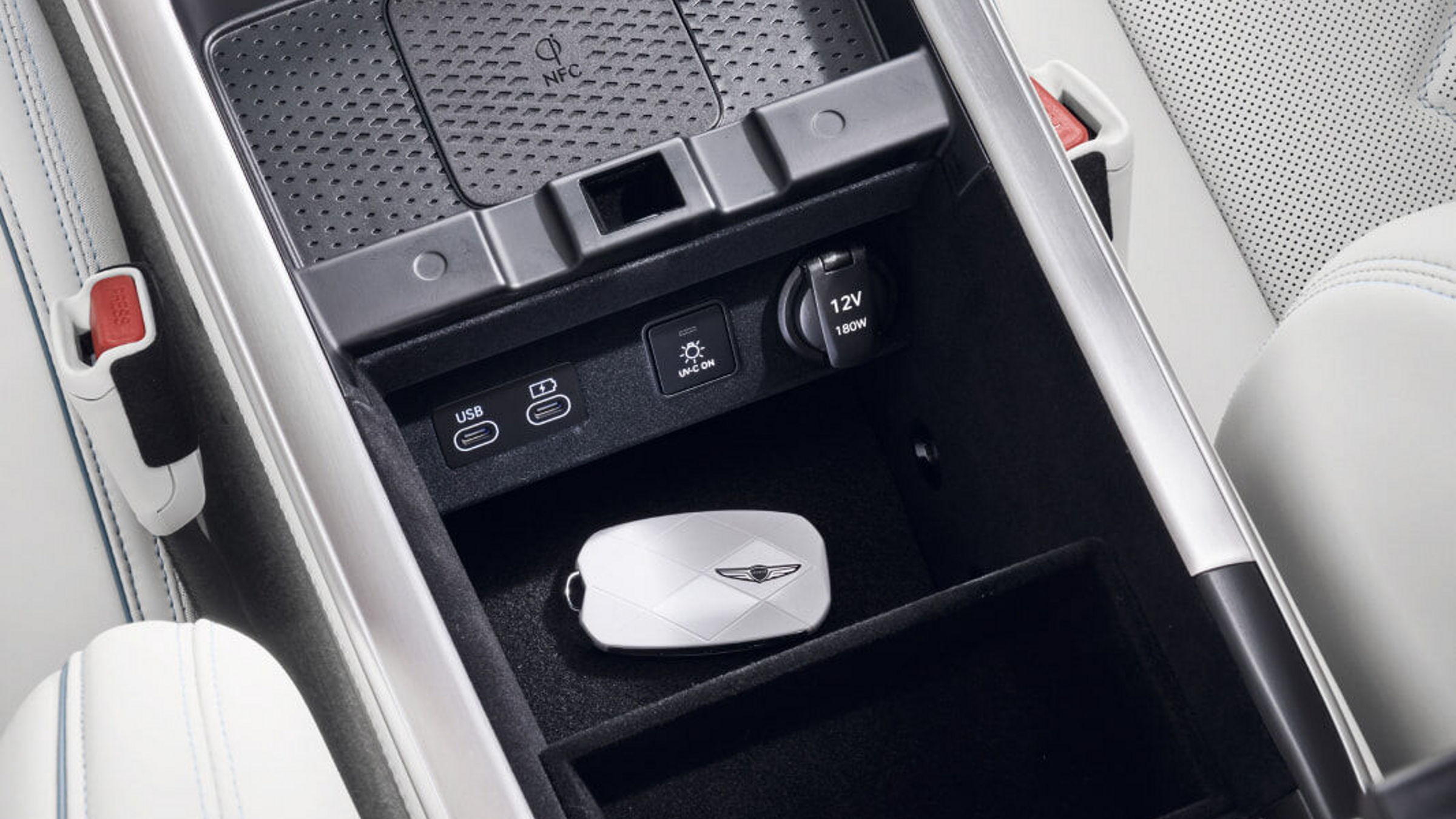 Consola central del Electrified GV70 con el área de almacenamiento, cargador inalámbrico, puertos USB-C, botón UV-C y la llave del vehículo.