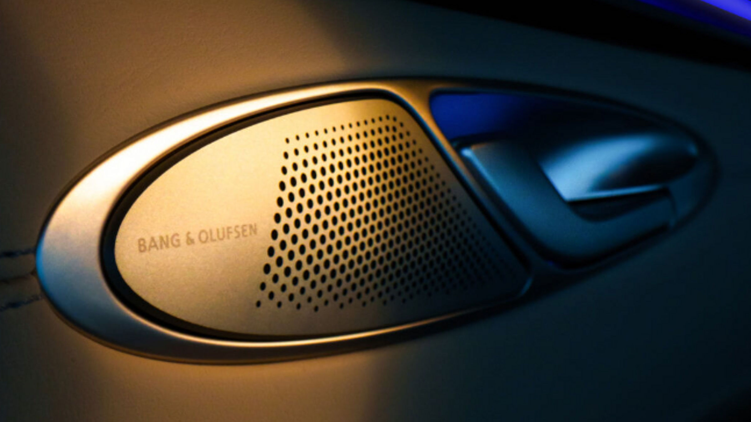 Detalle de la rejilla del altavoz Bang & Olufsen en el panel de la puerta, con iluminación ambiental.