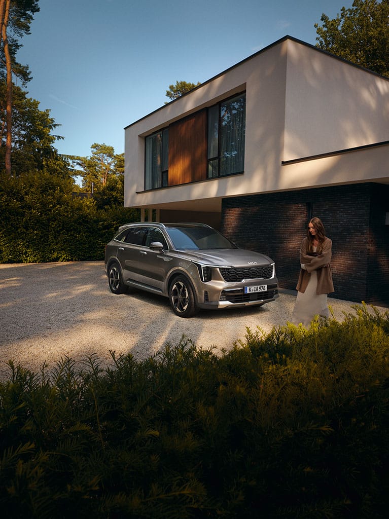 Kia Sorento gris oscuro aparcado en una entrada de grava frente a una casa moderna, con una persona a su lado