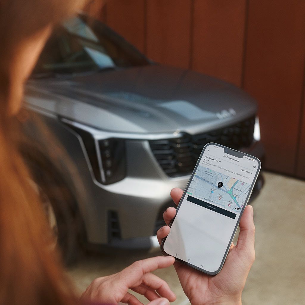 Persona sosteniendo un smartphone con una app de navegación y un Kia Sorento gris desenfocado al fondo