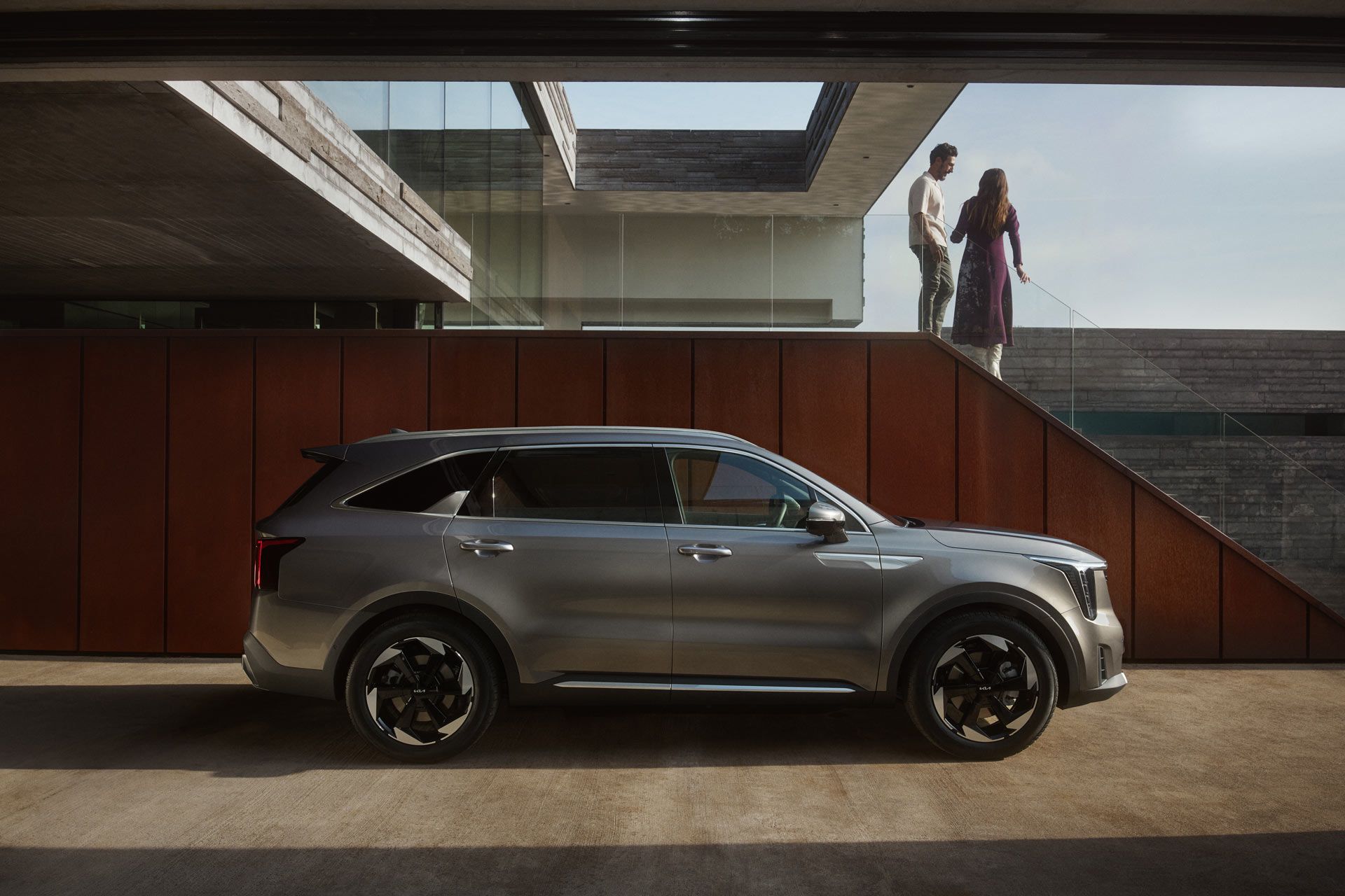 Vista lateral de un Kia Sorento gris oscuro estacionado frente a un edificio moderno, con llantas multirradio oscuras con detalles plateados
