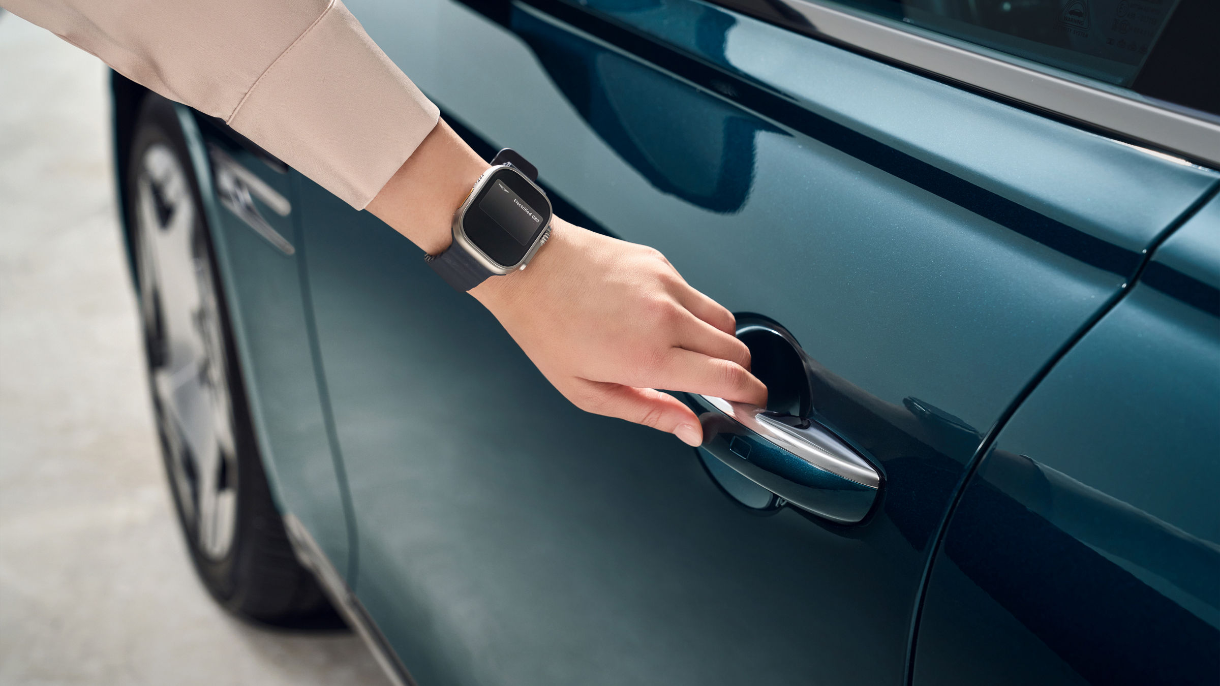 Mano con reloj inteligente mostrando Electrified G80 mientras abre la manilla de la puerta