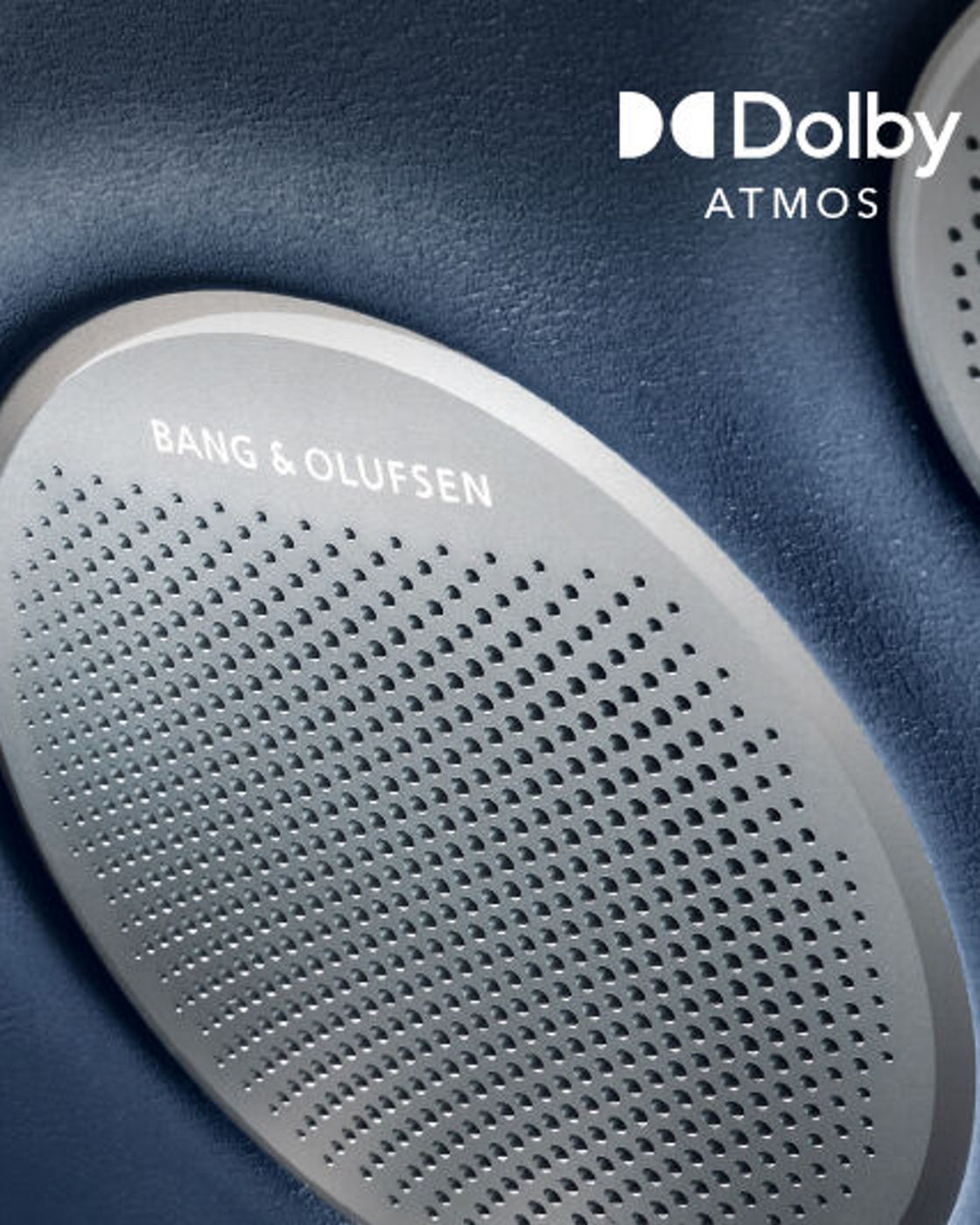 Primer plano de la rejilla de un altavoz Bang & Olufsen con distintivo Dolby Atmos sobre panel interior azul oscuro