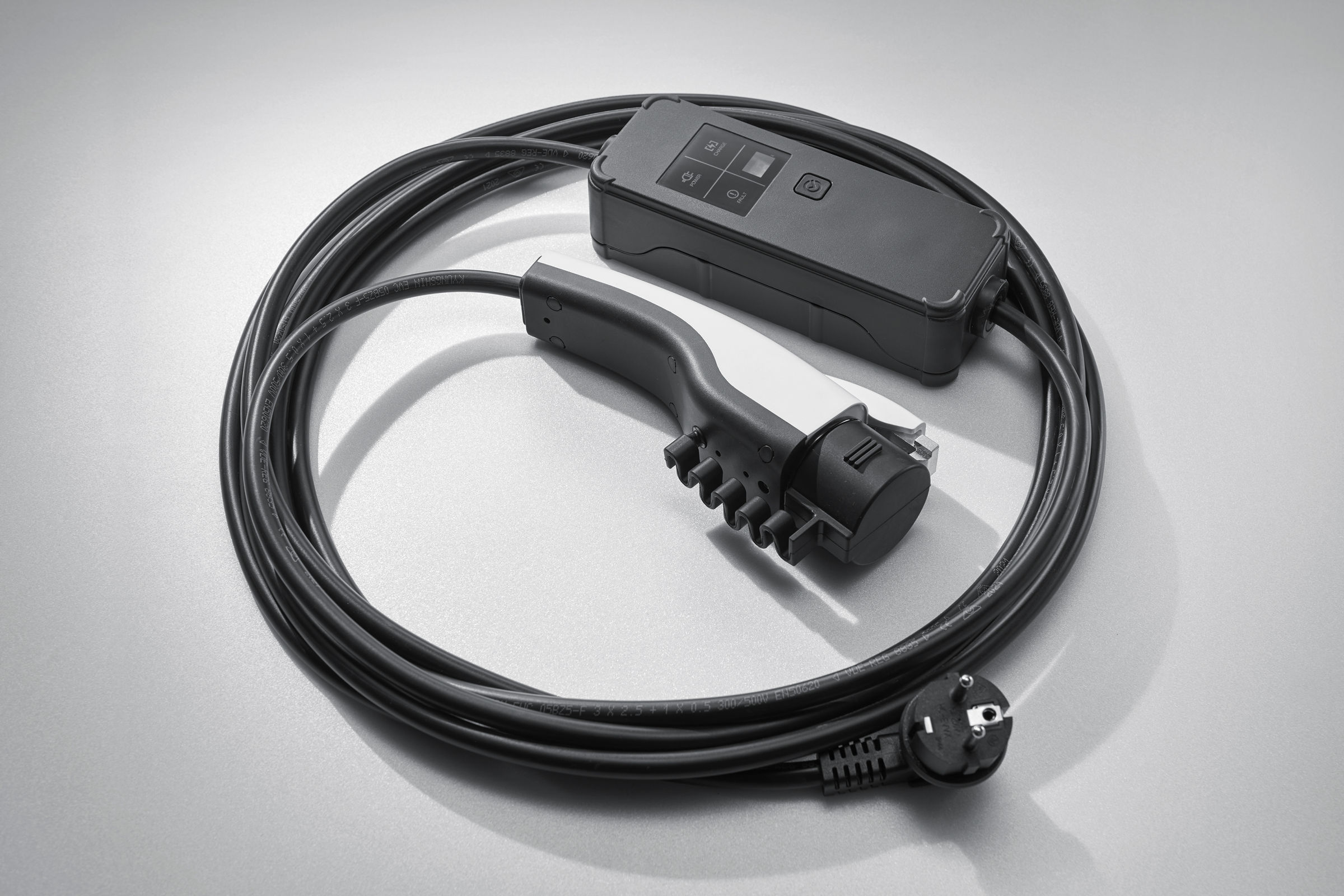Cable de carga para vehículo eléctrico con conectores, enrollado sobre superficie gris
