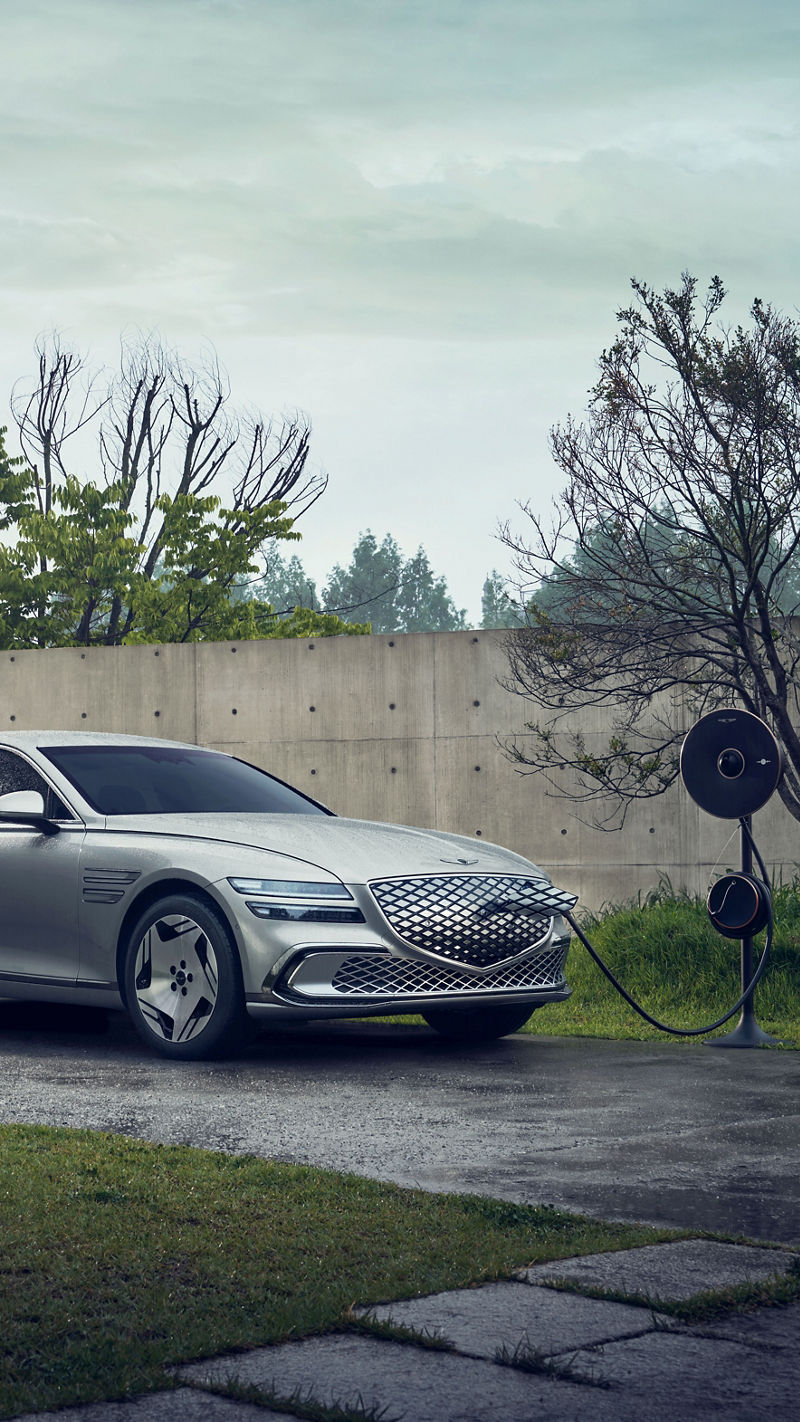 Electrified G80 plateado conectado a un cargador exterior en vista tres cuartos frontal